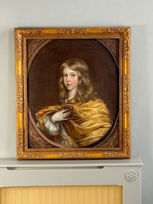 fig 3. A 17th-century oil portrait of a young boy with long curled hair draped in golden-yellow silk, set within a painted trompe loeil oval border.