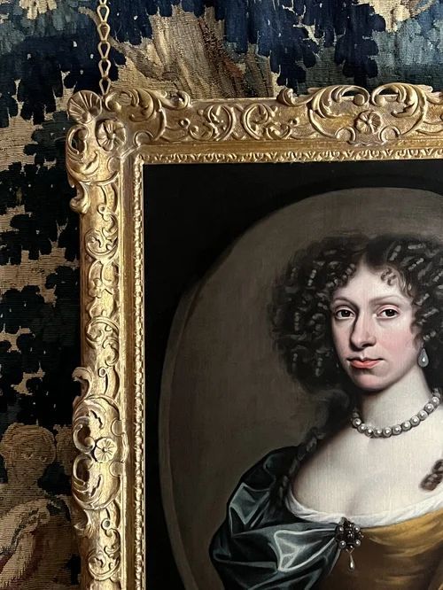 fig 1. A 17th-century oil portrait of a woman wearing a gold and blue gown with pearl jewellery, painted within a feigned oval canvas frame.