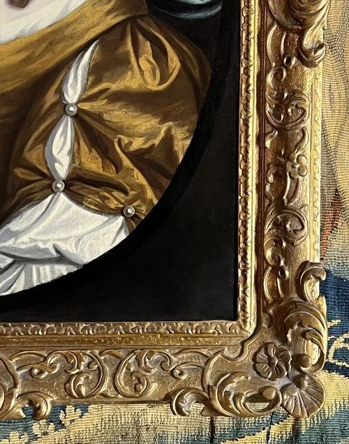 fig 7. A 17th-century oil portrait of a woman wearing a gold and blue gown with pearl jewellery, painted within a feigned oval canvas frame.
