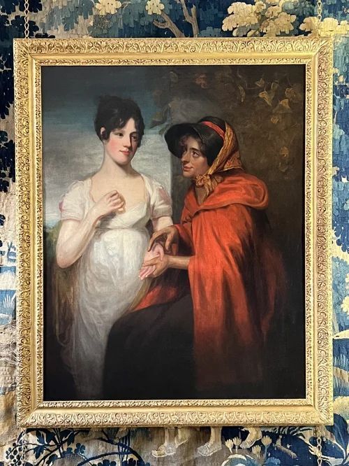 fig 1. An oil painting on canvas in an ornate gilt frame depicting a young lady in a white dress having her palm read by a fortune teller in a red hood.