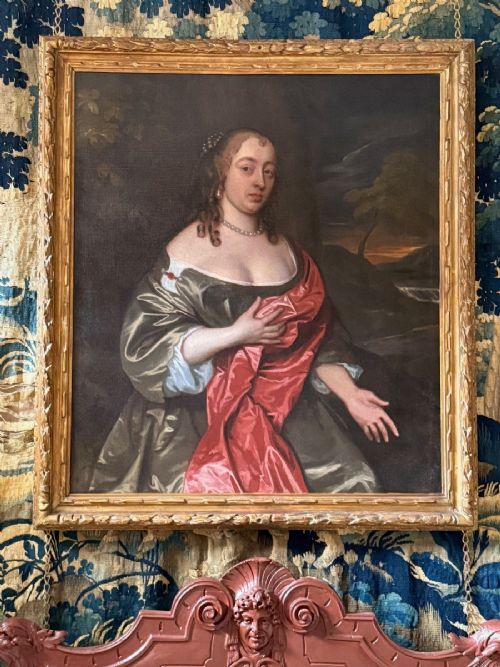 fig 6. An oil painting depicting a seated 17th-century lady in a green silk gown with red drapery against a natural landscape background.