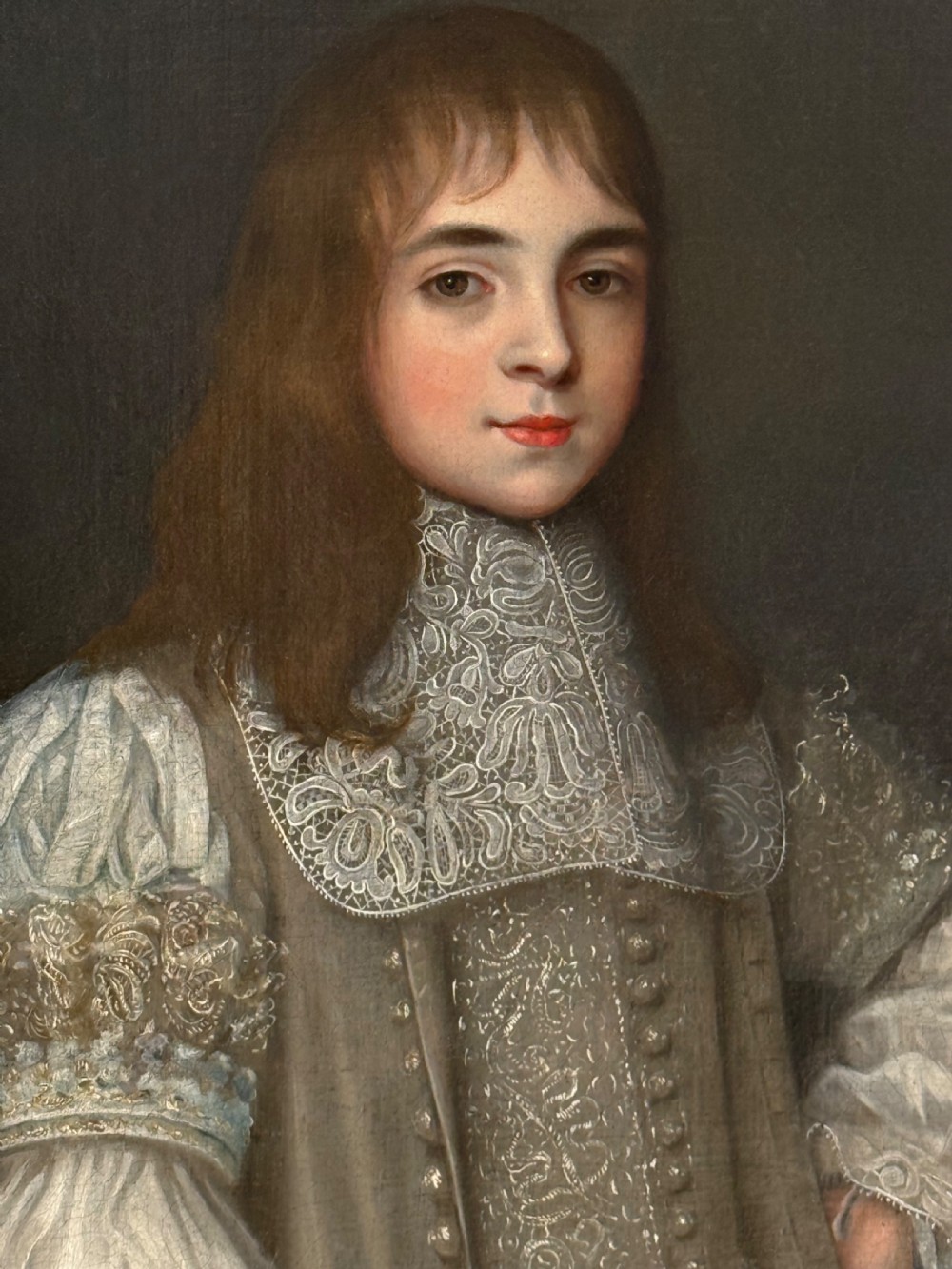 A seventeenth-century oil portrait depicting a young gentleman wearing an intricate lace collar and embroidered clothing in a carved silvered frame.