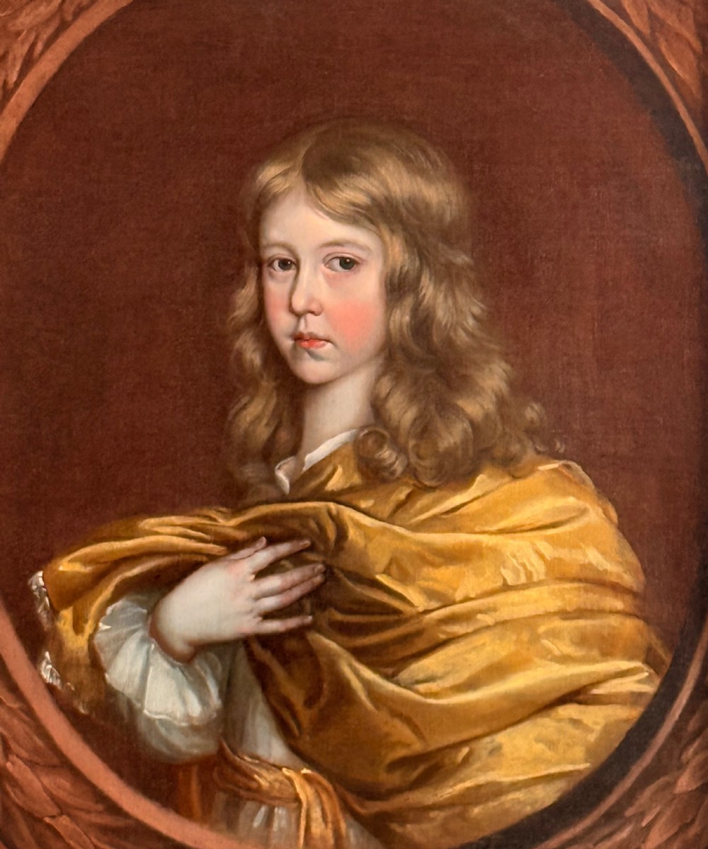 A 17th-century oil portrait of a young boy with long curled hair draped in golden-yellow silk, set within a painted trompe loeil oval border. View VI