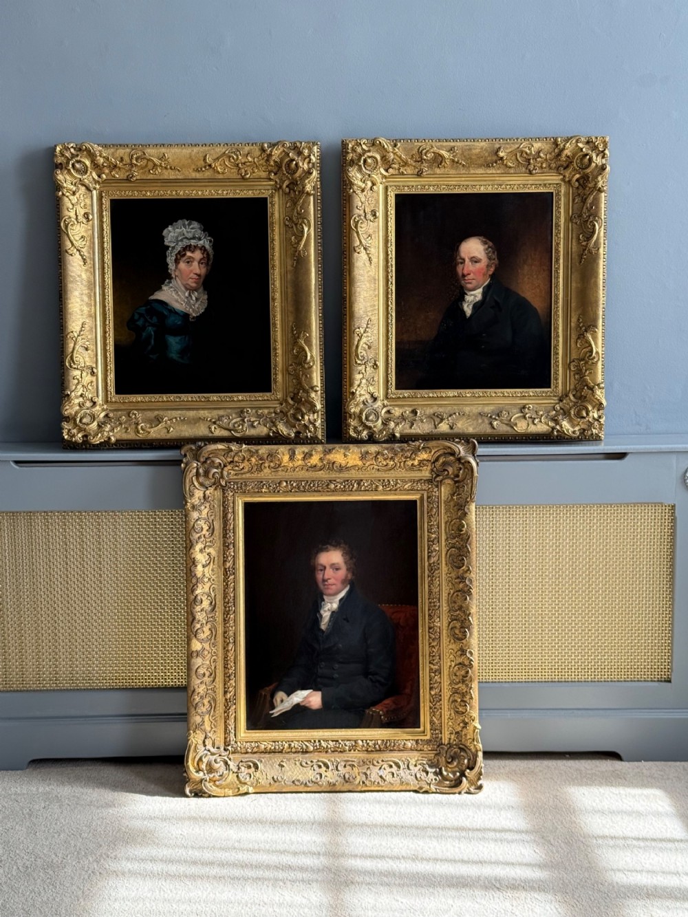 A set of three 19th-century Regency oil portraits painted on wood panels, housed in elaborate, heavily carved giltwood frames.