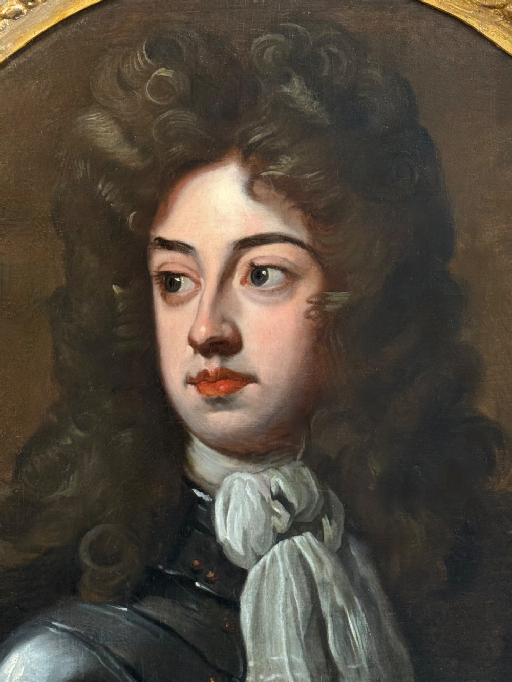 An oval late 17th-century oil portrait of a long-haired nobleman in dark plate armour with a white cravat, set within a carved gilt frame. View VI
