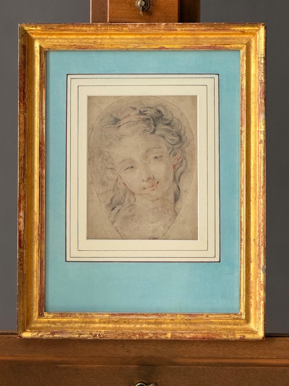 An 18th-century French Rococo chalk portrait drawing of a woman, displayed within a pale blue mount and an antique gilt frame. View II