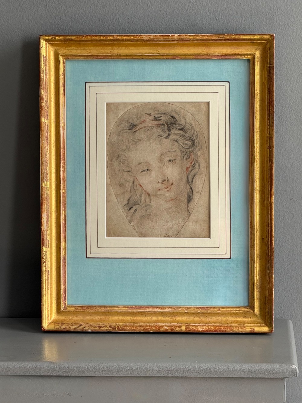 An 18th-century French Rococo chalk portrait drawing of a woman, displayed within a pale blue mount and an antique gilt frame. View V