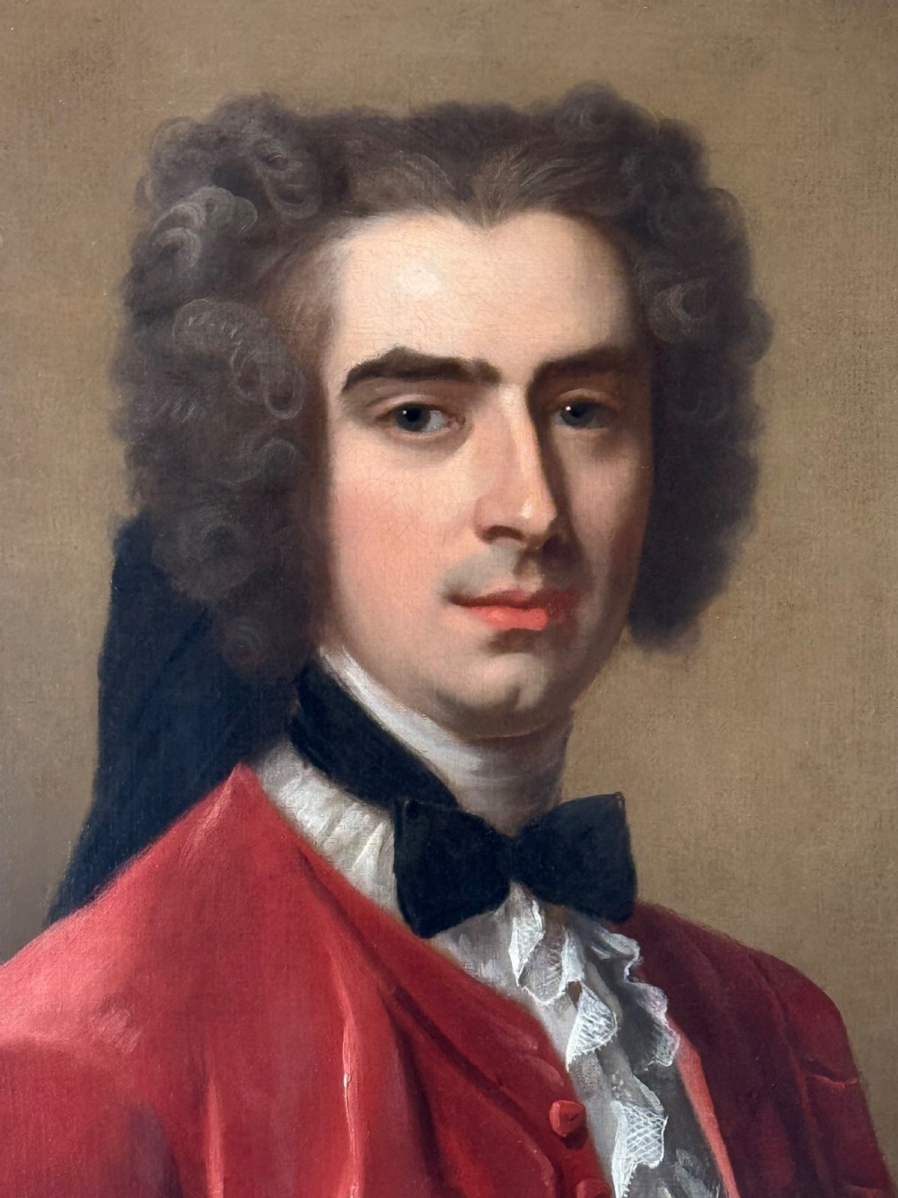 An 18th-century oil painting depicting a gentleman in a scarlet jacket with a white cravat, framed in an ornate gilded Rococo-style frame. View II