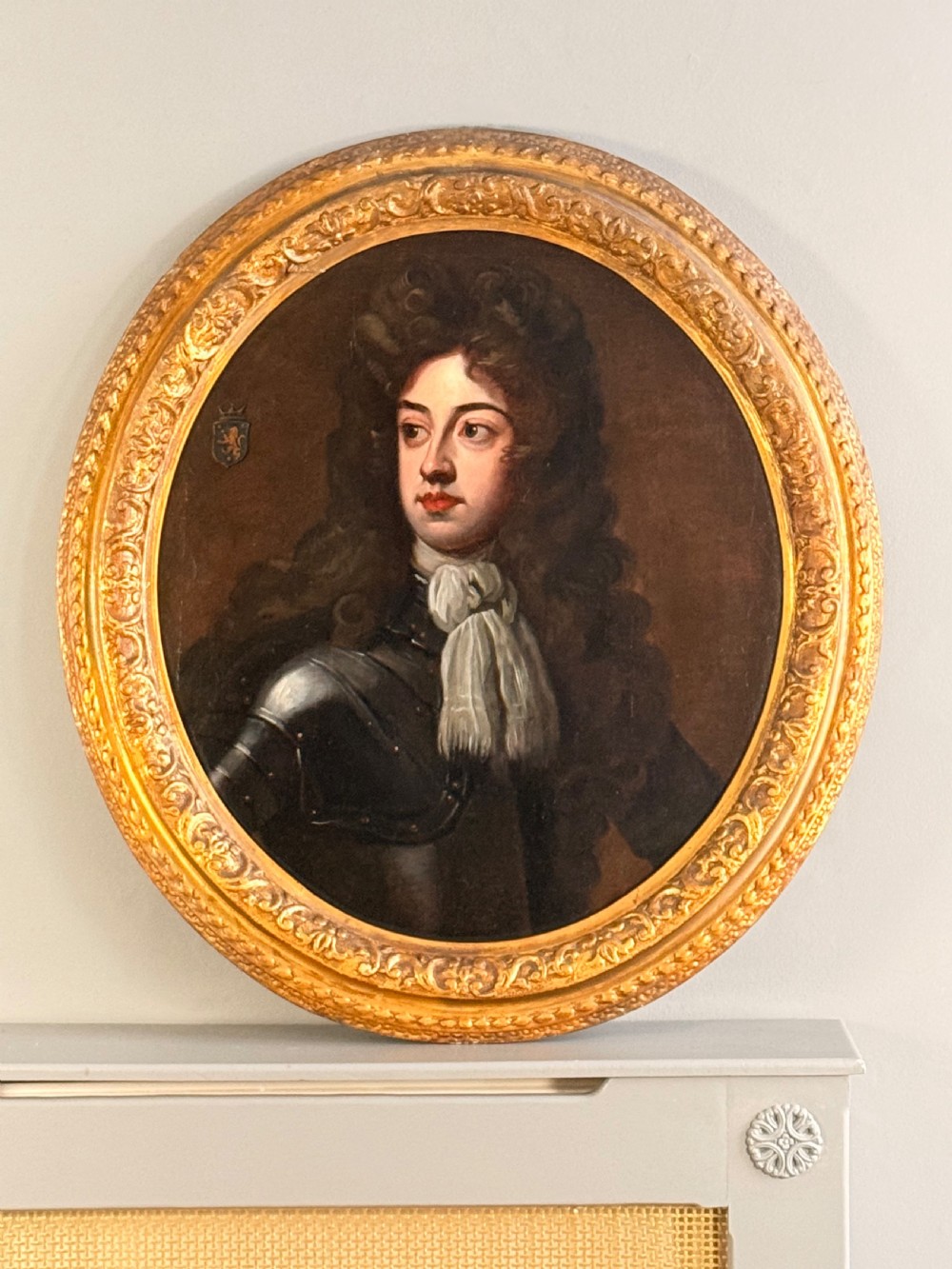 An oval Baroque oil portrait depicting a nobleman in plate armour with a white lace cravat and full wig, housed in a carved gilded frame.