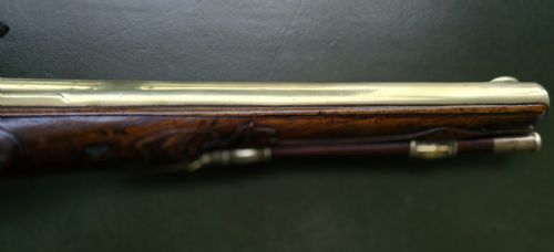 fig 2. An 18th-century French flintlock holster pistol featuring a carved walnut stock, polished brass barrel, engraved brass lockplate, and steel mechanism.