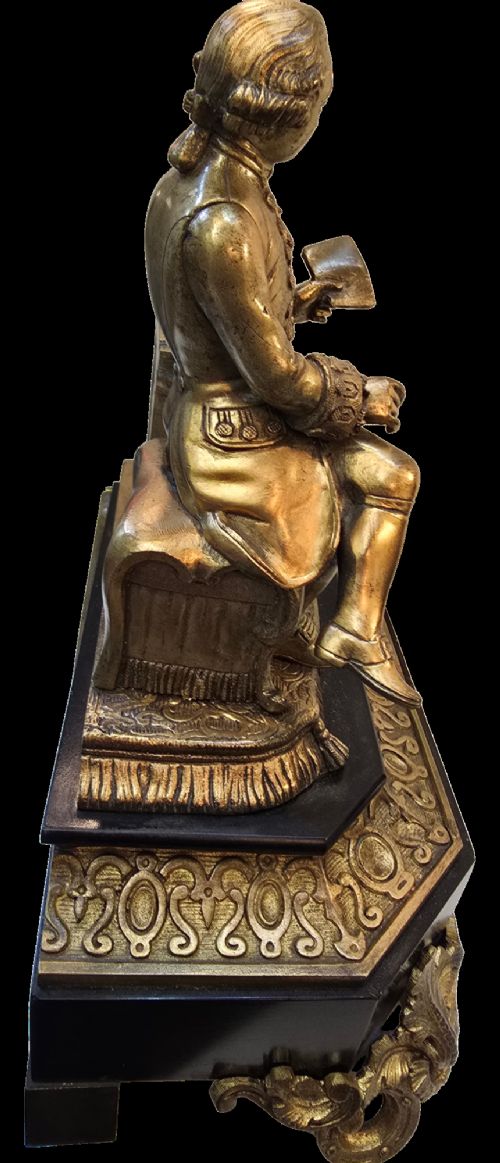 A 19th-century French gilt bronze sculpture depicting a seated gentleman in historic dress holding a quill, supported by an ornate black base with metallic scroll feet. View IX