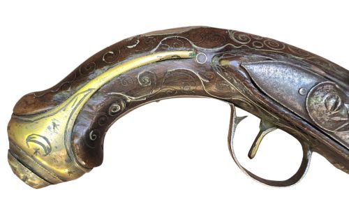 fig 2. An early 19th-century Ottoman Balkan flintlock holster pistol featuring a dark wood stock inlaid with silver wire scrollwork and a cast brass pommel.