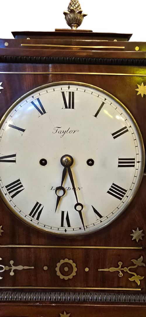 A Georgian mahogany bracket clock featuring brass star and floral motifs, a pineapple finial, brass ball feet, and a white dial marked Taylor London with Roman numerals. View VII