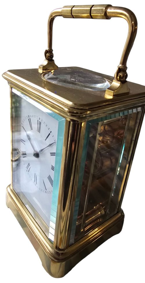 A rectangular French gilt-brass carriage clock featuring bevelled glass panels, a white enamel dial with Roman numerals, and a hinged top handle. View XII