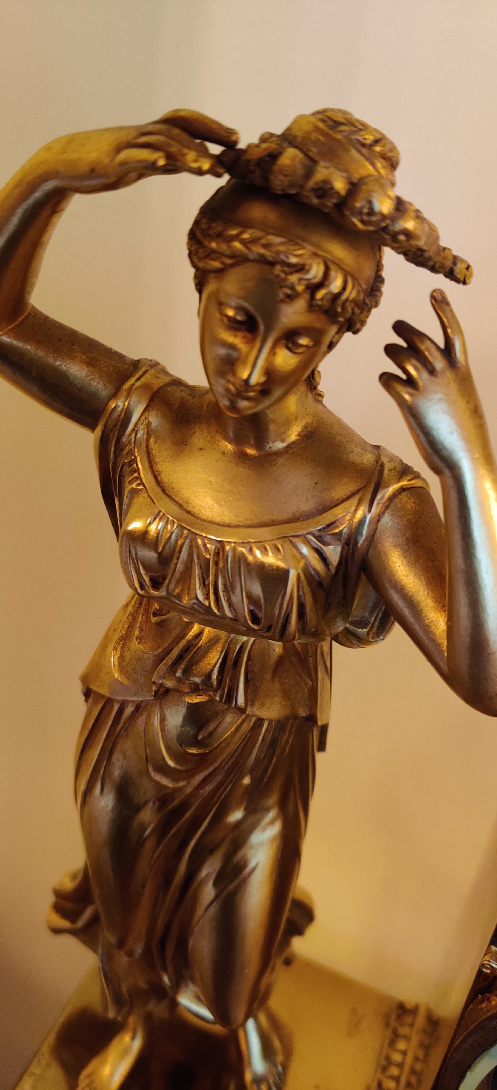 A 19th-century French gilt bronze figural mantel clock featuring a draped female classical figure beside a rectangular clock casing topped with an ornate urn finial. View IX