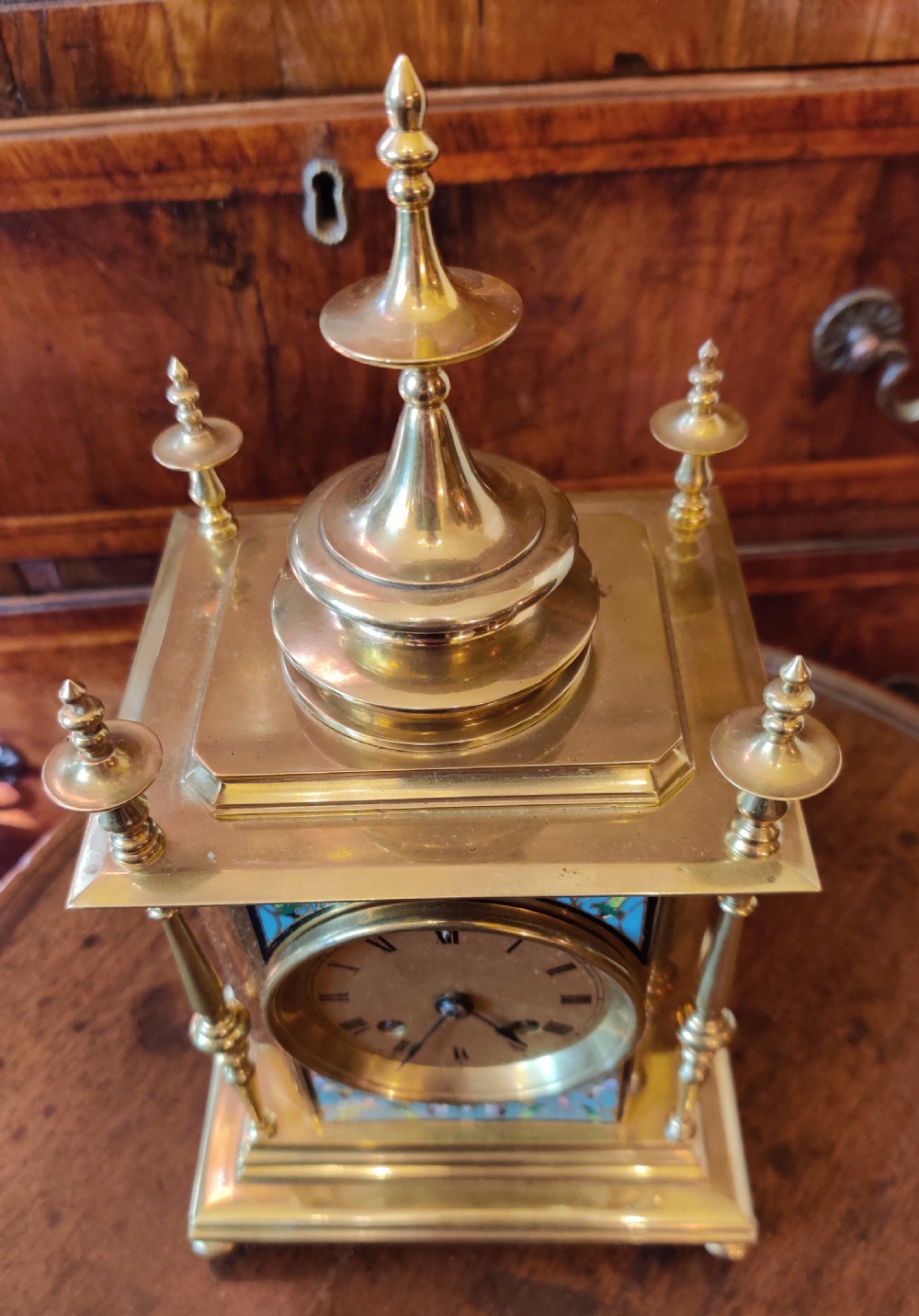 An antique brass mantel clock featuring turquoise and polychrome champleve enamel work framing a central Roman numeral dial, topped with decorative finials. View IX