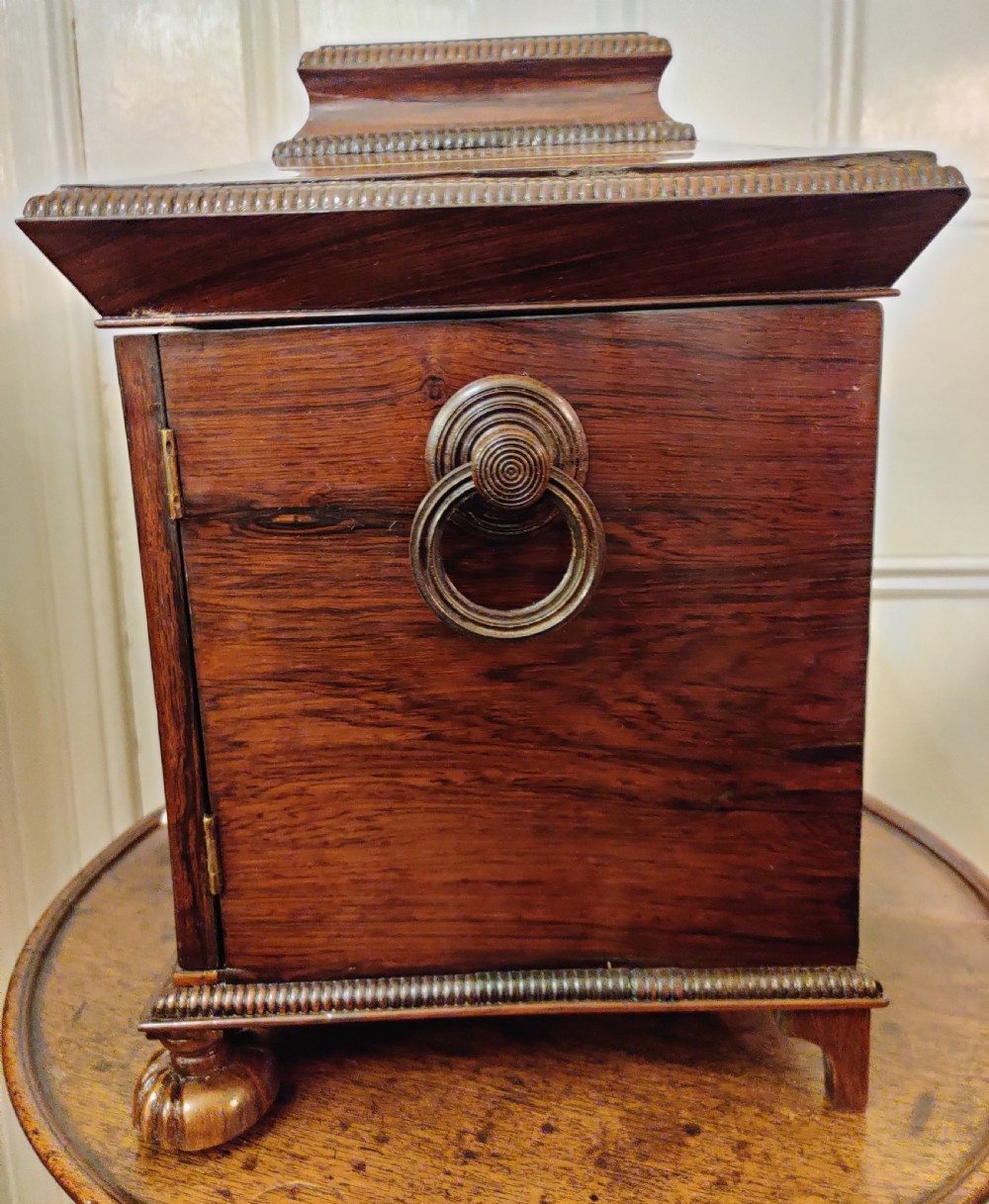 A Georgian dark rosewood tabletop cabinet featuring mother of pearl inlay, a sarcophagus-shaped top, side brass handles, and carved feet. View VII