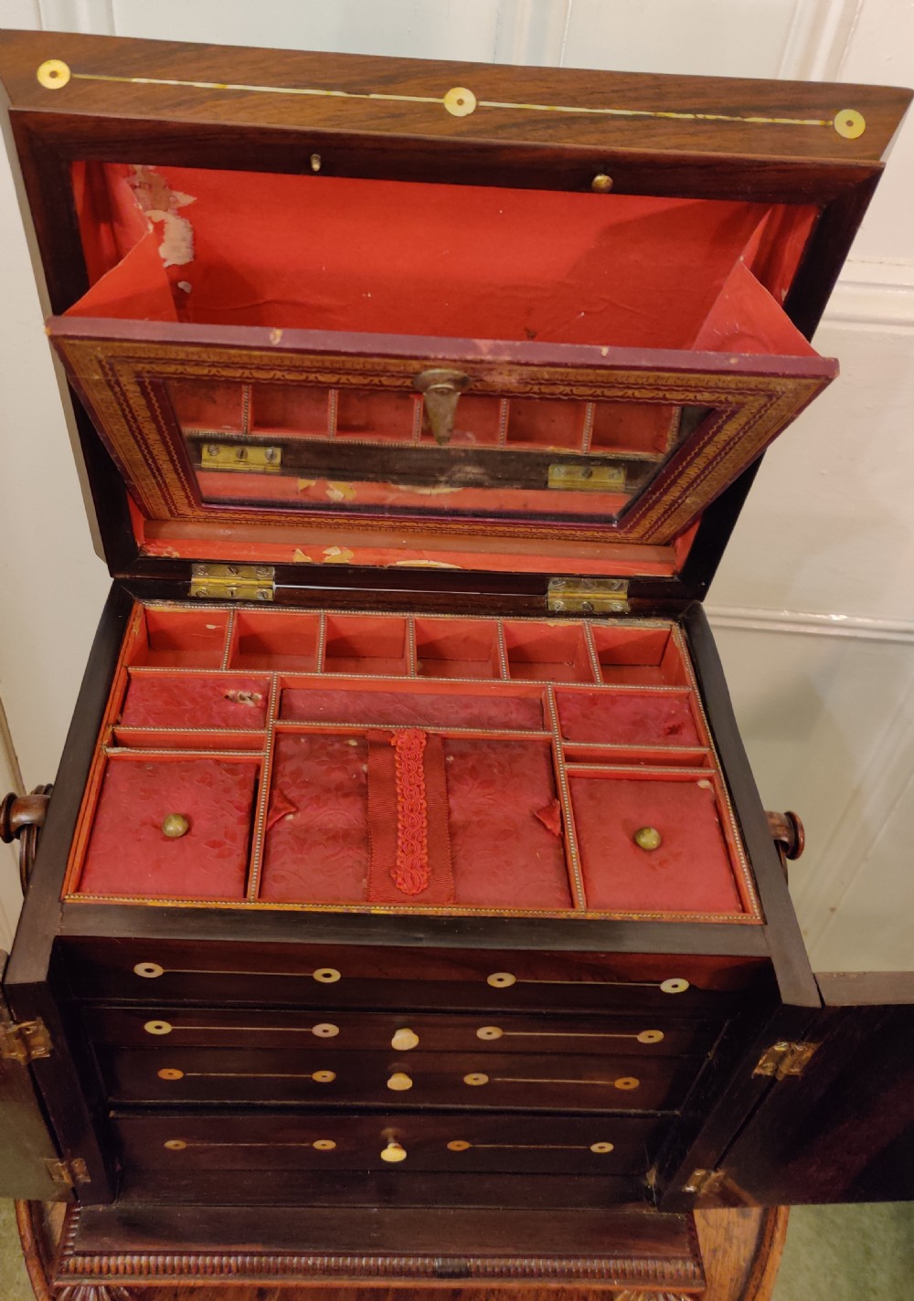 A Georgian dark rosewood tabletop cabinet featuring mother of pearl inlay, a sarcophagus-shaped top, side brass handles, and carved feet. View X