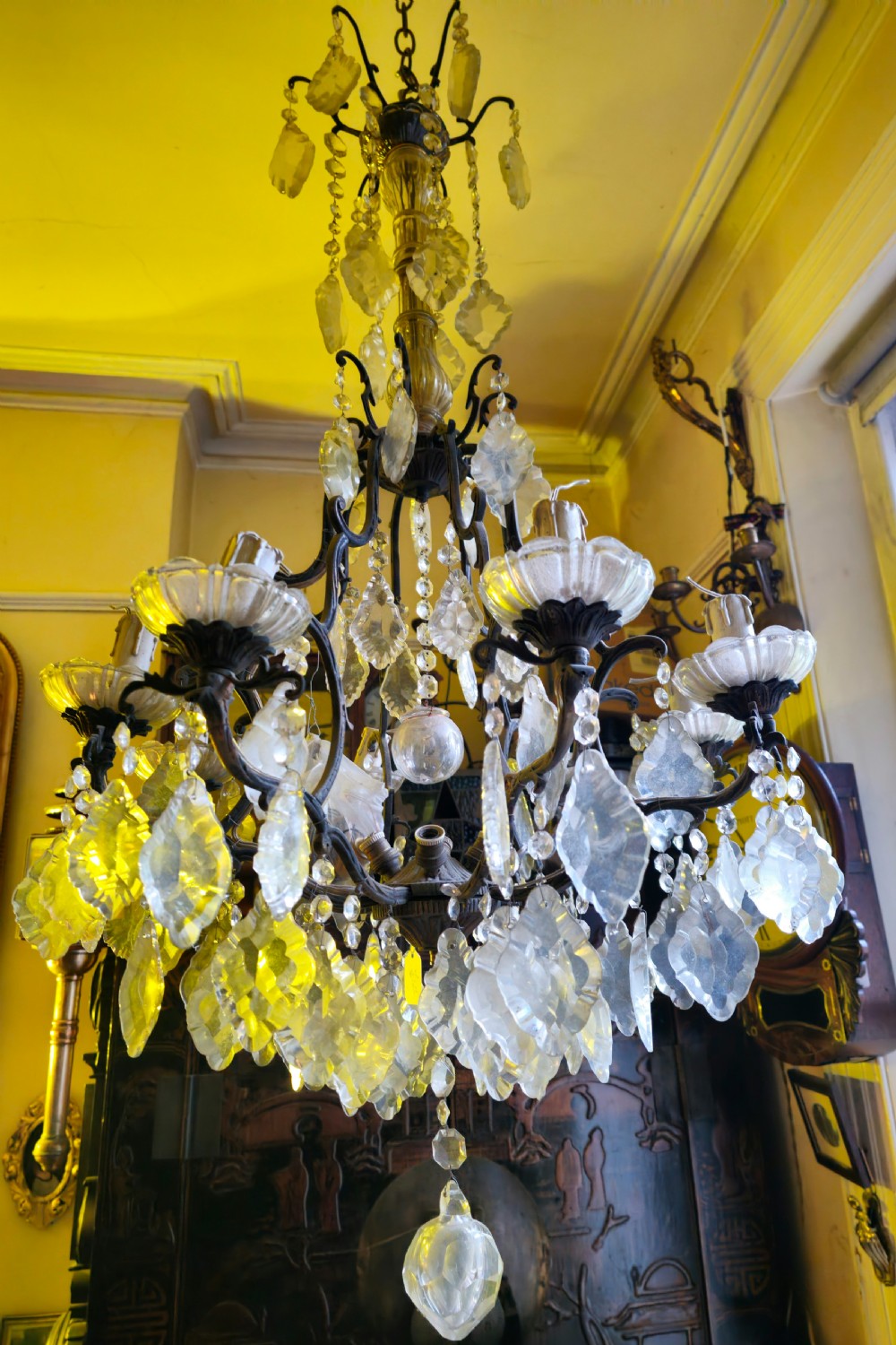 A French circa 1910 multi-tiered chandelier featuring dark metal scrollwork, scalloped glass bobeches, and numerous faceted cut-glass drops.
