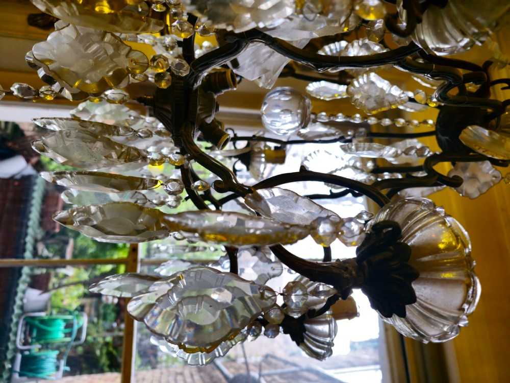 A French circa 1910 multi-tiered chandelier featuring dark metal scrollwork, scalloped glass bobeches, and numerous faceted cut-glass drops. View II