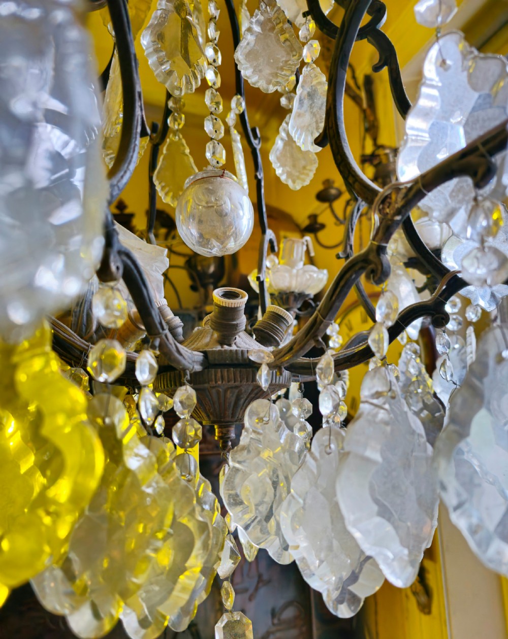 A French circa 1910 multi-tiered chandelier featuring dark metal scrollwork, scalloped glass bobeches, and numerous faceted cut-glass drops. View VII