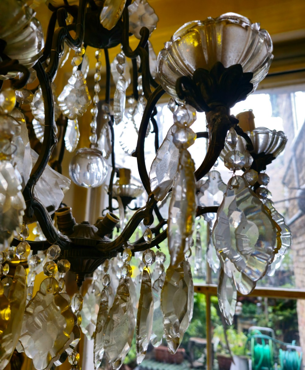 A French circa 1910 multi-tiered chandelier featuring dark metal scrollwork, scalloped glass bobeches, and numerous faceted cut-glass drops. View VIII