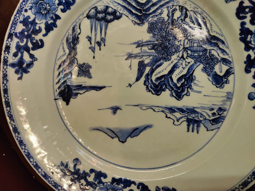 A circular 18th-century Chinese blue and white porcelain plate featuring a central hand-painted river landscape surrounded by a floral rim pattern. View VIII