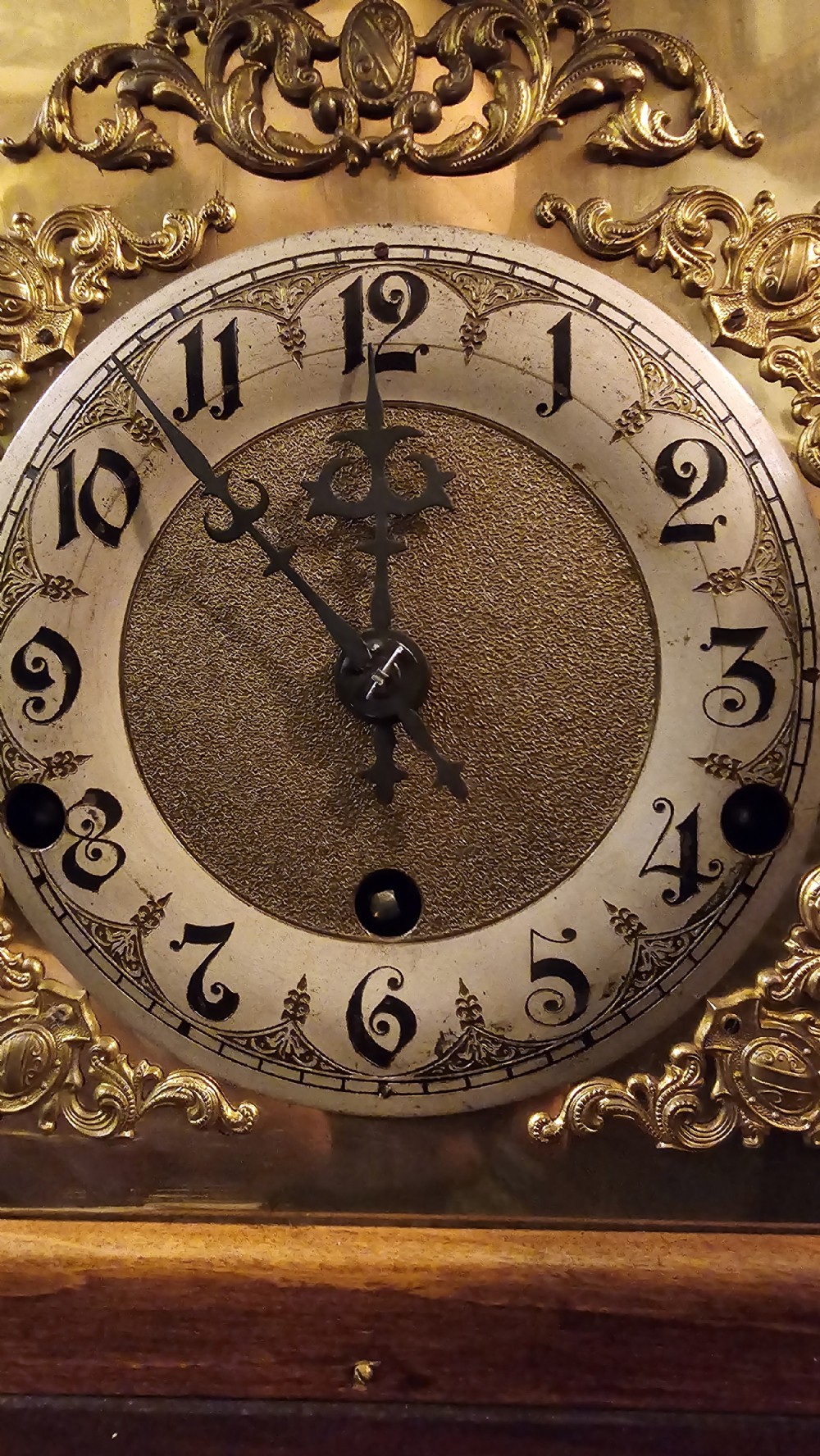 An antique wooden mantel clock featuring a carved walnut architectural case, a brass dial with decorative spandrels, and finial accents. View XII