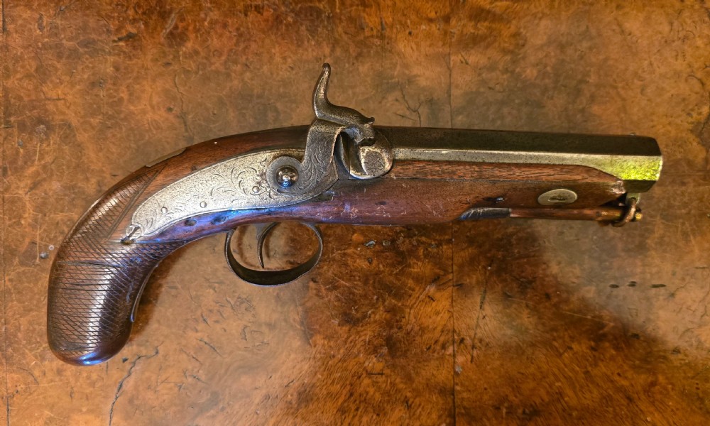 An 1840s percussion belt pistol featuring an engraved steel lockplate, octagonal barrel, and a carved walnut stock with a cross-hatched grip. View XX