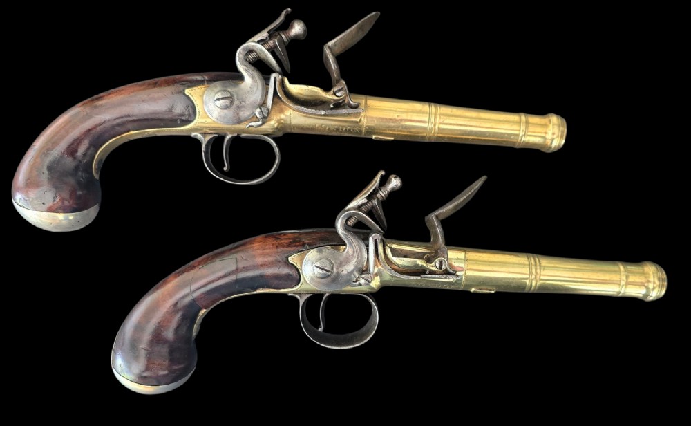 A pair of 18th-century English flintlock turn-off pistols featuring brass cannon barrels, steel lock mechanisms, and smooth walnut stocks.