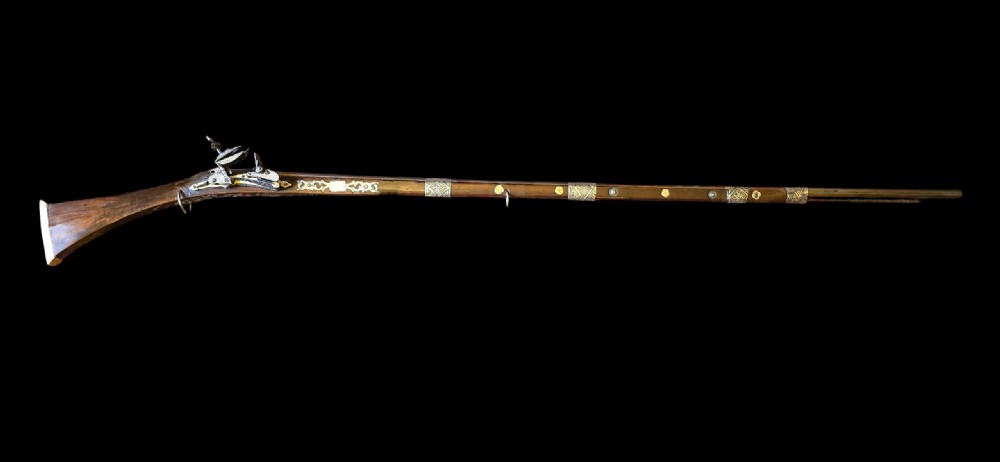 An 18th century Ottoman Algerian toe-lock long gun featuring a slender wooden stock decorated with brass bands and bone inlays.