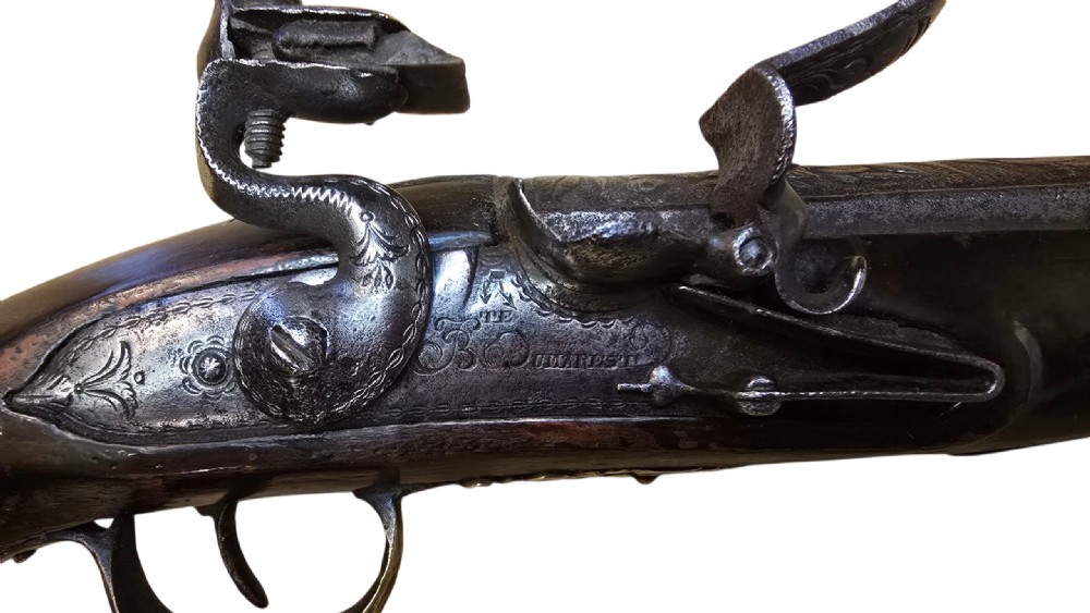 An antique Ottoman flintlock pistol featuring a dark carved wooden stock inlaid with silver accents and a steel barrel with gilt detailing. View II
