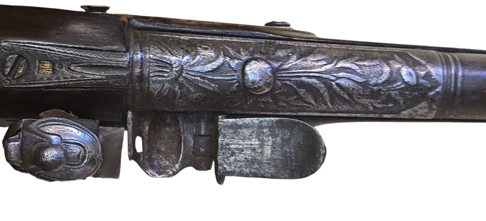 An antique Ottoman flintlock pistol featuring a dark carved wooden stock inlaid with silver accents and a steel barrel with gilt detailing. View III