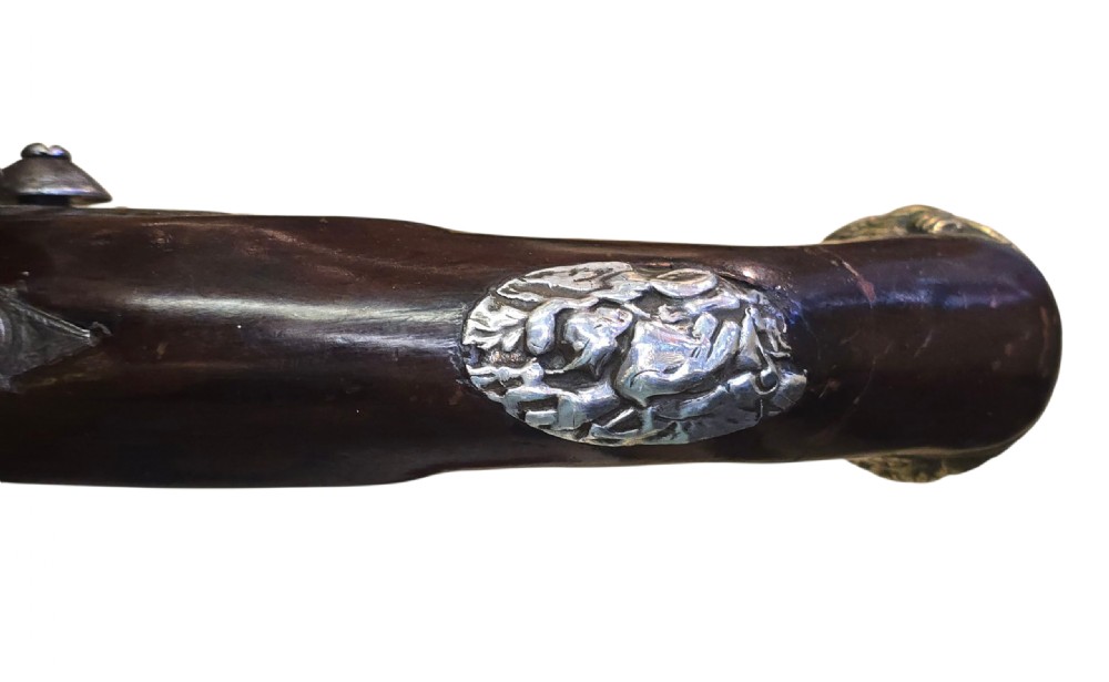 An antique Ottoman flintlock pistol featuring a dark carved wooden stock inlaid with silver accents and a steel barrel with gilt detailing. View IV