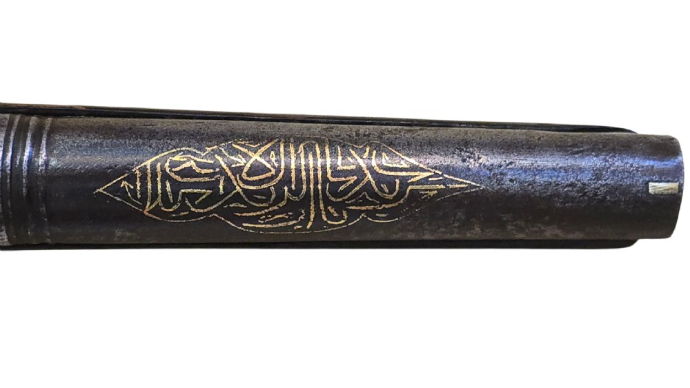 An antique Ottoman flintlock pistol featuring a dark carved wooden stock inlaid with silver accents and a steel barrel with gilt detailing. View V