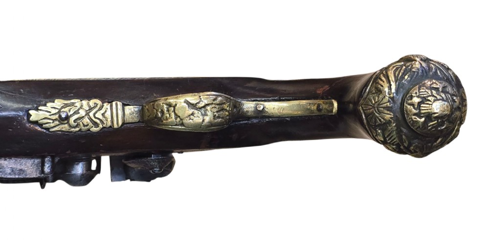 An antique Ottoman flintlock pistol featuring a dark carved wooden stock inlaid with silver accents and a steel barrel with gilt detailing. View VII