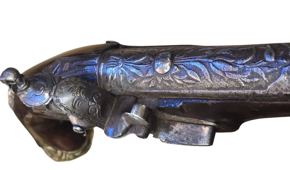 An antique Ottoman flintlock pistol featuring a dark carved wooden stock inlaid with silver accents and a steel barrel with gilt detailing. View IX
