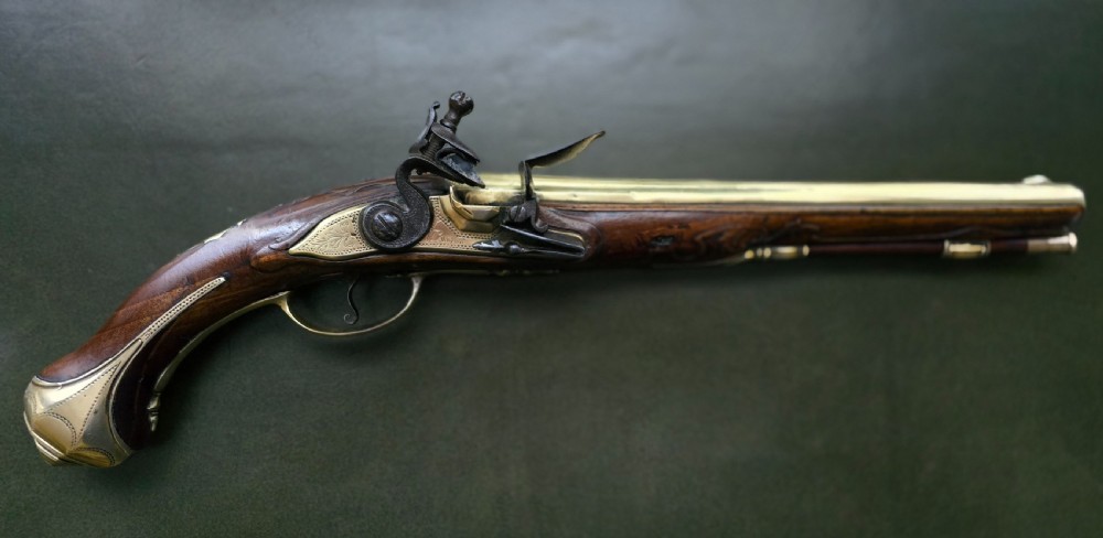 An 18th-century French flintlock holster pistol featuring a carved walnut stock, polished brass barrel, engraved brass lockplate, and steel mechanism.