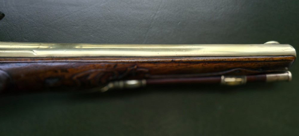 An 18th-century French flintlock holster pistol featuring a carved walnut stock, polished brass barrel, engraved brass lockplate, and steel mechanism. View III