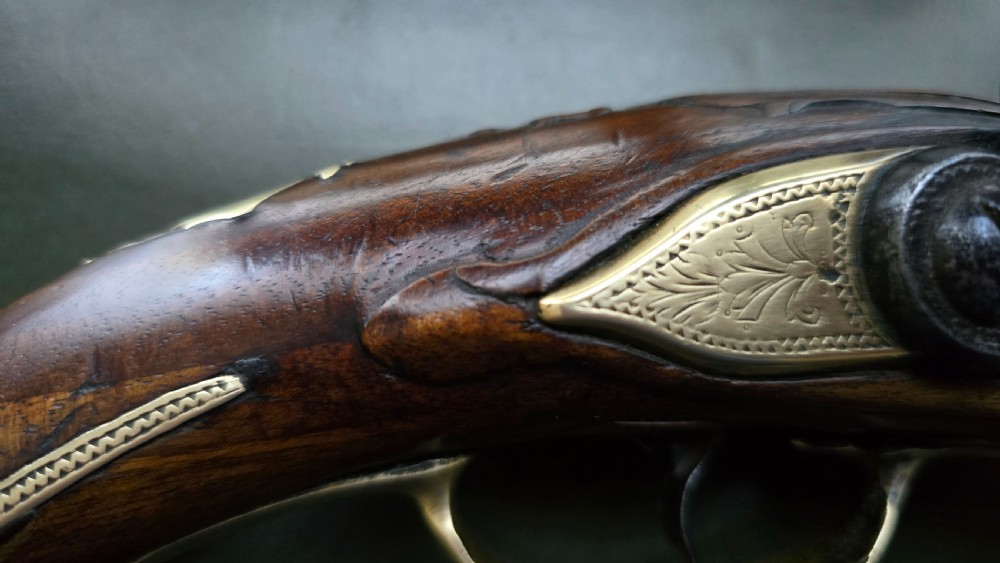 An 18th-century French flintlock holster pistol featuring a carved walnut stock, polished brass barrel, engraved brass lockplate, and steel mechanism. View VI