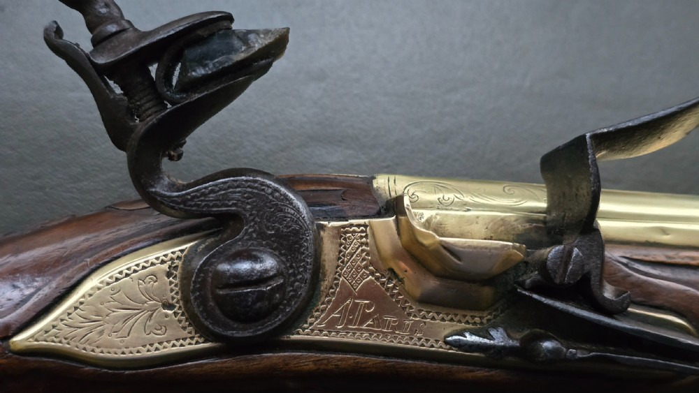 An 18th-century French flintlock holster pistol featuring a carved walnut stock, polished brass barrel, engraved brass lockplate, and steel mechanism. View VII