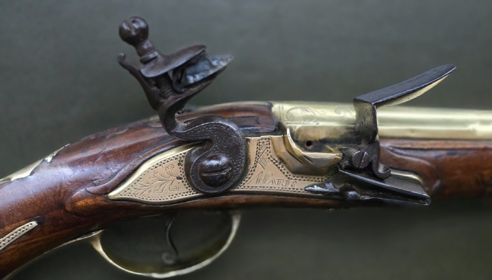 An 18th-century French flintlock holster pistol featuring a carved walnut stock, polished brass barrel, engraved brass lockplate, and steel mechanism. View VIII