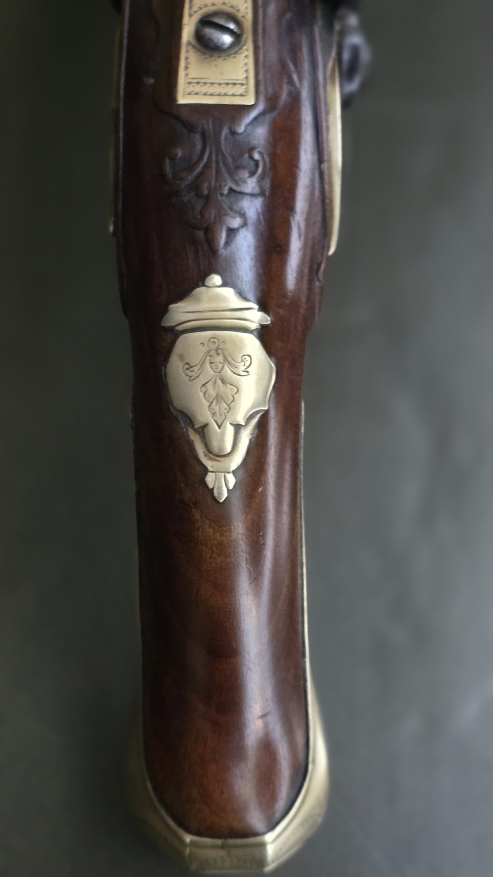 An 18th-century French flintlock holster pistol featuring a carved walnut stock, polished brass barrel, engraved brass lockplate, and steel mechanism. View IX