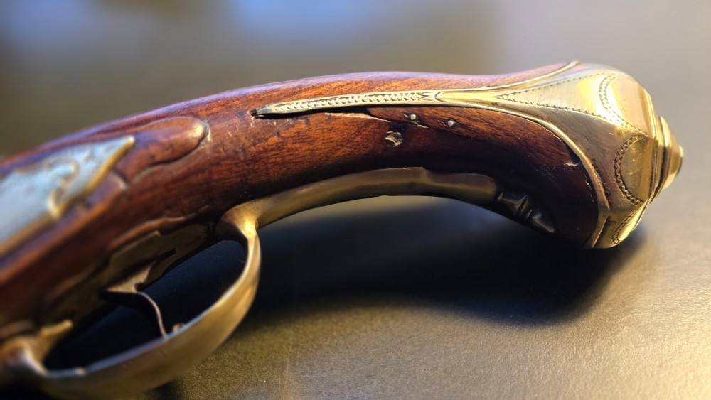 An 18th-century French flintlock holster pistol featuring a carved walnut stock, polished brass barrel, engraved brass lockplate, and steel mechanism. View XV