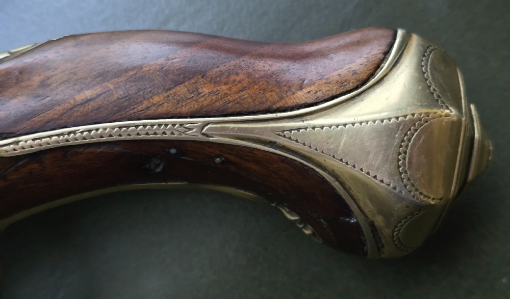 An 18th-century French flintlock holster pistol featuring a carved walnut stock, polished brass barrel, engraved brass lockplate, and steel mechanism. View XVI