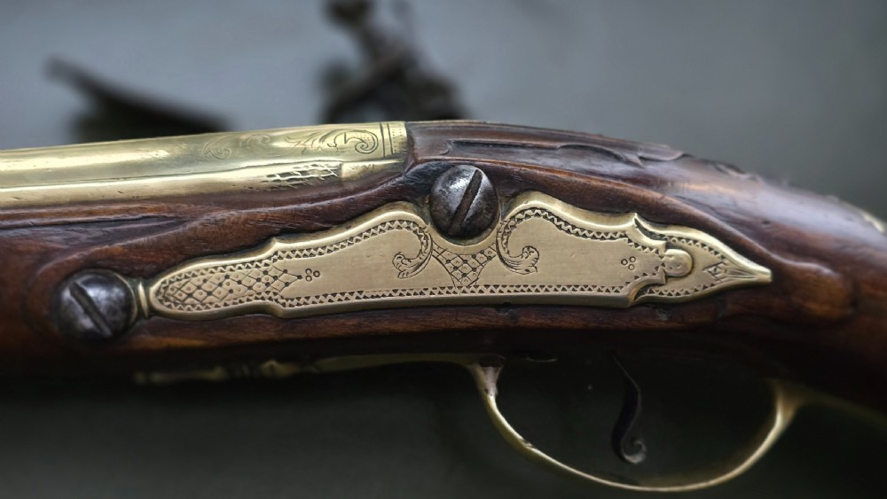 An 18th-century French flintlock holster pistol featuring a carved walnut stock, polished brass barrel, engraved brass lockplate, and steel mechanism. View XVII