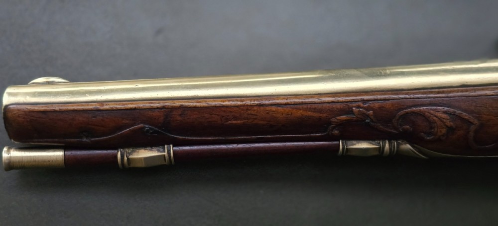 An 18th-century French flintlock holster pistol featuring a carved walnut stock, polished brass barrel, engraved brass lockplate, and steel mechanism. View XIX
