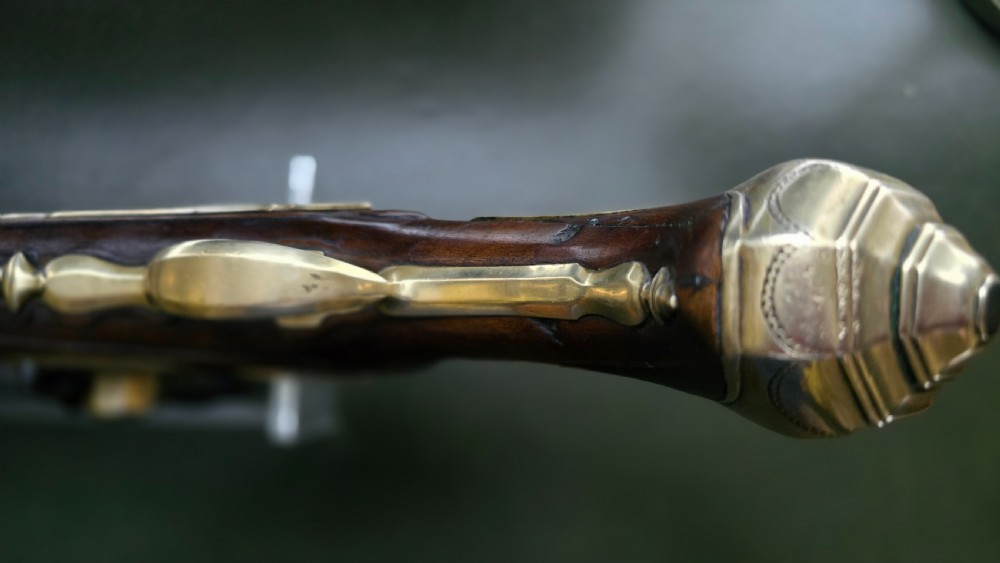 An 18th-century French flintlock holster pistol featuring a carved walnut stock, polished brass barrel, engraved brass lockplate, and steel mechanism. View XXI