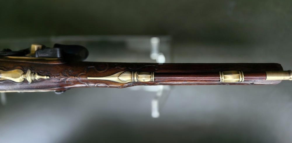 An 18th-century French flintlock holster pistol featuring a carved walnut stock, polished brass barrel, engraved brass lockplate, and steel mechanism. View XXII