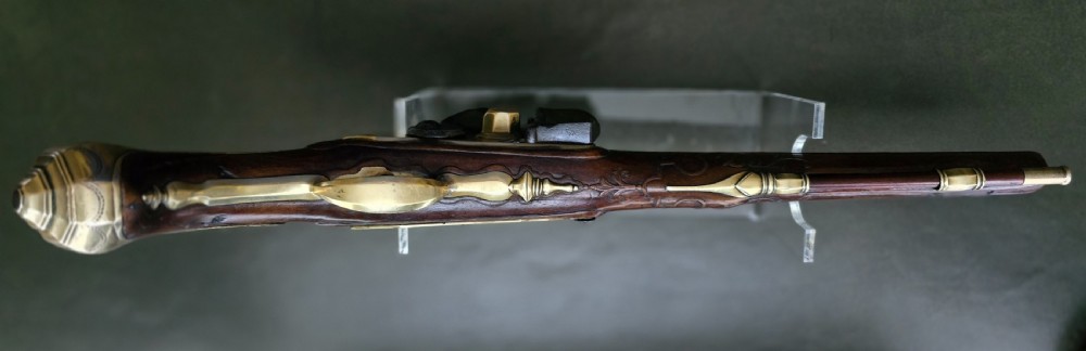 An 18th-century French flintlock holster pistol featuring a carved walnut stock, polished brass barrel, engraved brass lockplate, and steel mechanism. View XXIII